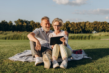Joyful elder couple relaxing outdoors with digital tablet - 767884829