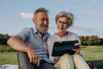 Portrait of joyful elder couple relaxing outdoors with digital tablet - 767884835