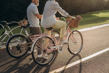 Joyful pensioners pedaling vintage bicycles at summer park - 767884840