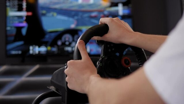 Close-up of a teenage boy wearing virtual reality glasses sitting in a car driving simulator in front of a large screen.