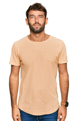 Handsome young man with beard wearing casual tshirt relaxed with serious expression on face. simple...