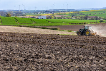 A tractor cultivates a plowed field in the spring