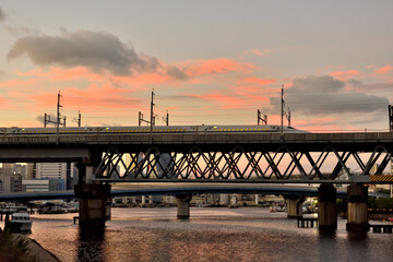 夕日に染まる京浜運河を横切る鉄橋を渡る新幹線