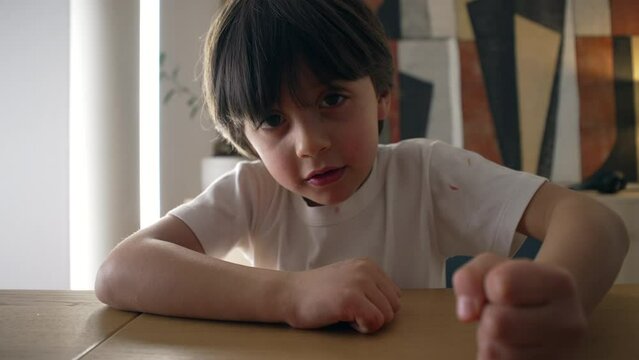 Assertive child hits table surface with hand. 5 year old boy demanding attention while looking at camera, close-up face and fist