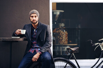 Portrait, city and man drinking coffee with bicycle at cafe table for breakfast in the morning. Bike, tea cup and serious person with espresso, latte or beverage at restaurant with winter fashion - Powered by Adobe