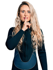 Young blonde woman wearing diver neoprene uniform asking to be quiet with finger on lips. silence...