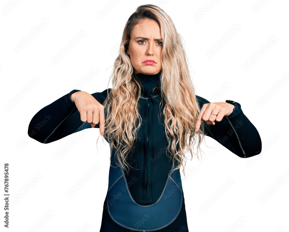 Poster Young blonde woman wearing diver neoprene uniform pointing down looking sad and upset, indicating direction with fingers, unhappy and depressed.