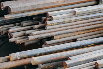 A pile of rusty metal rods. The rods are stacked on top of each other and are all different sizes. Scene is somewhat bleak and industrial, as the rods appear to be old and worn