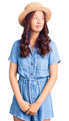 Young beautiful chinese girl wearing summer hat smiling looking to the side and staring away thinking.