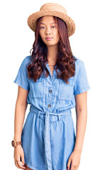 Young beautiful chinese girl wearing summer hat relaxed with serious expression on face. simple and natural looking at the camera.