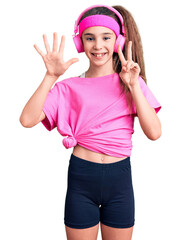 Cute hispanic child girl wearing gym clothes and using headphones showing and pointing up with fingers number seven while smiling confident and happy.
