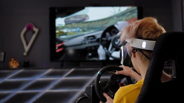 A teenager is playing a racing car game with virtual reality glasses in front of a big screen. Car driving simulator in the game room.