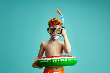 Red Haired Child Boy With Inflatable Circle, Mask and Snorkel for Diving Standing on Blue Isolated...