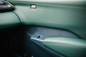 Button to open or close window and door in new modern sedan automobile. Opener from inside. Gold luxury button in green leather interior in electric car. Supercar interior design detail.