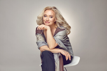 Attractive mature blonde woman in her fifties wearing in casual clothing and stylish plaid holds...