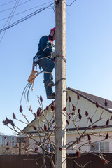 an electrician man in overalls and a red helmet climbs onto an electric pole to install an electric line
