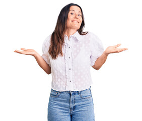 Young beautiful brunette woman wearing casual shirt clueless and confused expression with arms and...