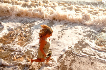 Fototapeta premium A beautiful large in a turquoise sundress walks alonf the seashore against the sand beach and sea or ocean