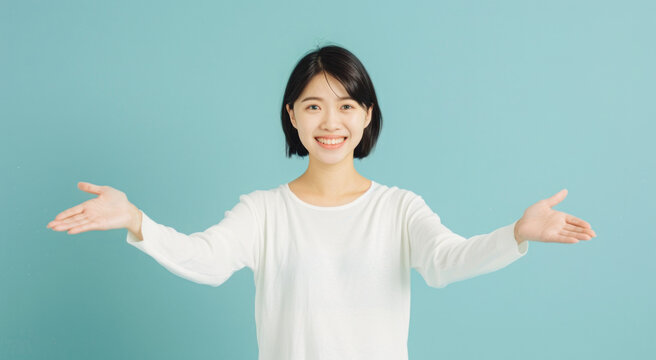 Warm Asian lady in white shirt and jeans, with arms wide open, invites you into her office space with a smile.