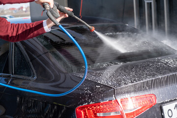 A man washes off the foam while washing the car. A vehicle is engulfed in soapy foam during a car...