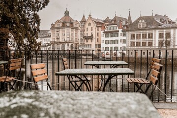 Terrace with outdoor furniture covered by snow in background of water near buildings in Luzern