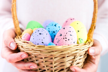 Woman's hands hold decorative Easter Eggs in a wicker basket. Easter decor. Close-up. Selective focus.
