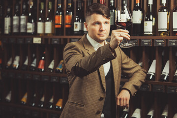 Sommelier looks at red wine in glass in cellar