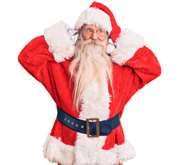 Old senior man with grey hair and long beard wearing traditional santa claus costume smiling...