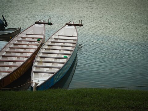 Image of a tranquil lake scene featuring a line of boats docked along the shoreline