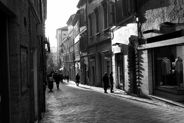 Obraz premium People walking through a quiet street in Macerata, Italy, captured in black and white