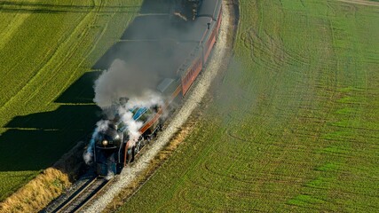 Industrial locomotive train in motion, driving through a green field emitting a plume of steam