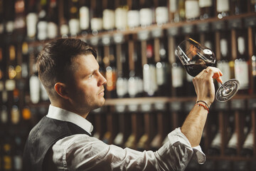 Male sommelier tasting red wine at cellar.