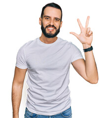 Young man with beard wearing casual white t shirt showing and pointing up with fingers number three while smiling confident and happy.