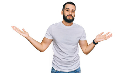 Young man with beard wearing casual white t shirt clueless and confused expression with arms and hands raised. doubt concept. - obrazy, fototapety, plakaty
