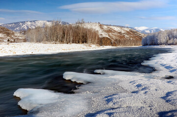 A frozen river bank with a distant mountain under a cloudy sky