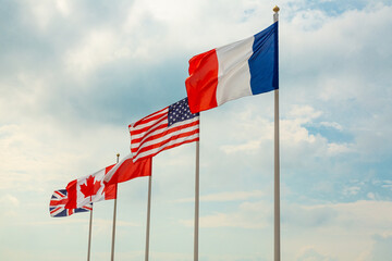 Flags France, USA Polish, Canada and Great Britain blow in the wind against a blue sky. D Day Hel,...