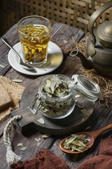 Vertical of dried senna in a bowl with a cup of tea on a wooden table
