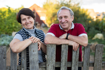 Elderly couple standing together near wooden fence in garden
