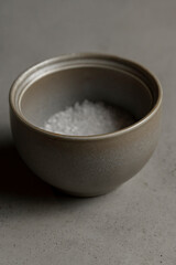Coarse salt in a ceramic bowl on a gray background, selective focus