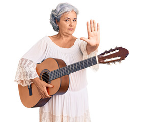 Senior woman with gray hair playing classical guitar with open hand doing stop sign with serious and confident expression, defense gesture