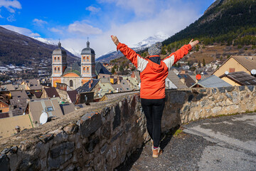 Young woman admiring the Collegiate Church of Our Lady and Saint Nicholas of Briançon from the top of the fortified old town built by Vauban in the French Alps - obrazy, fototapety, plakaty