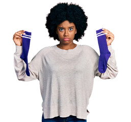 Young african american woman holding socks skeptic and nervous, frowning upset because of problem....