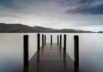 Wooden pier extending into a tranquil lake beneath a cloudy sky
