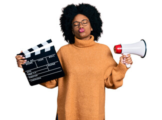 Young african american woman holding video film clapboard and megaphone looking at the camera...