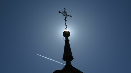 Blue sky with an airplane soaring against a tall church tower with a cross.