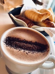 breakfast photo of a cup of hot chocolate served with croissants on a table on a sunny morning