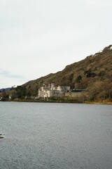 Scenic view of Kylemore Abbey situated on a hilltop, with a tranquil lake in the foreground.