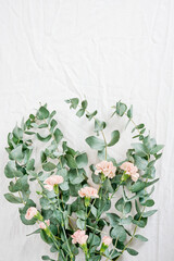 bouquet of eucalyptus leaves, pink carnations on white fabric background, still life, minimalism