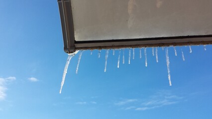 icicles on visor of roof of wooden house in spring day - 767956033