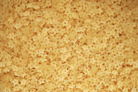 Macaroni stars texture. Italian pasta stellini for soup. Yellow small raw noodles in the shape of a star. Quality photo. Close-up